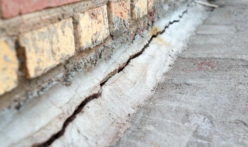 long crack in the concrete along the bottom of a tan brick home