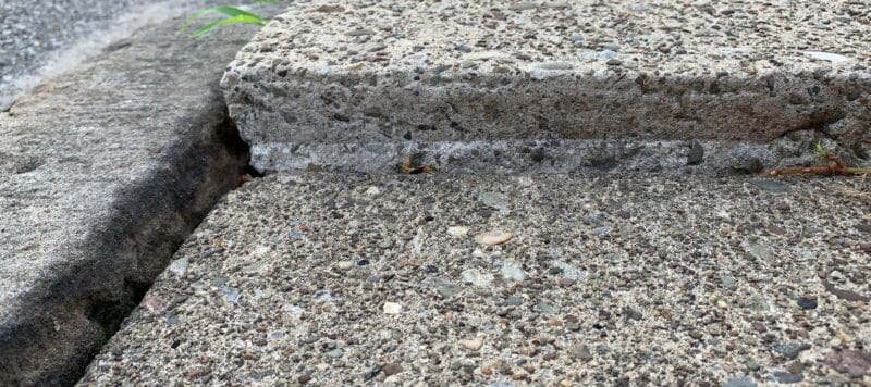 close up of groove between sidewalk squares. one is lifted much higher than the other