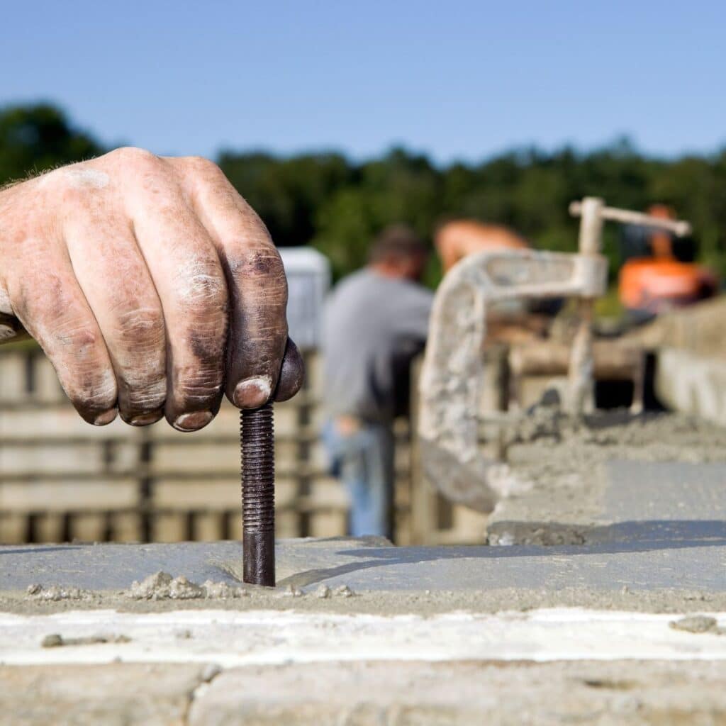 hand placing an anchor in a concrete foundation that has been recently poured