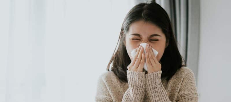 young woman sneezing into a tissue